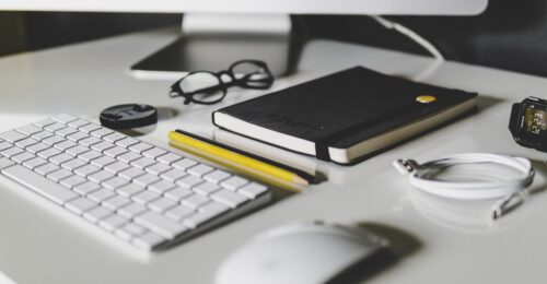 Minimalist workspace with an iMac, keyboard, notebook, and stationery.