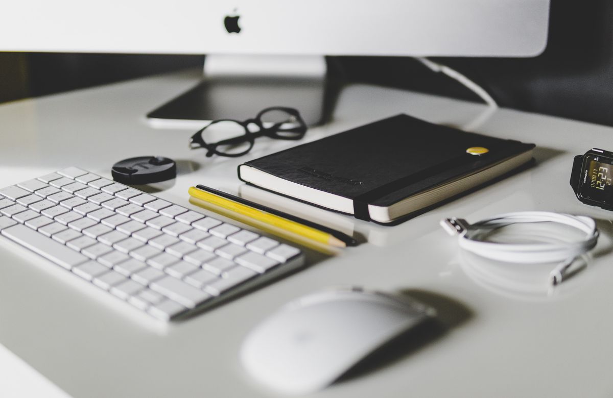 Minimalist workspace with an iMac, keyboard, notebook, and stationery.